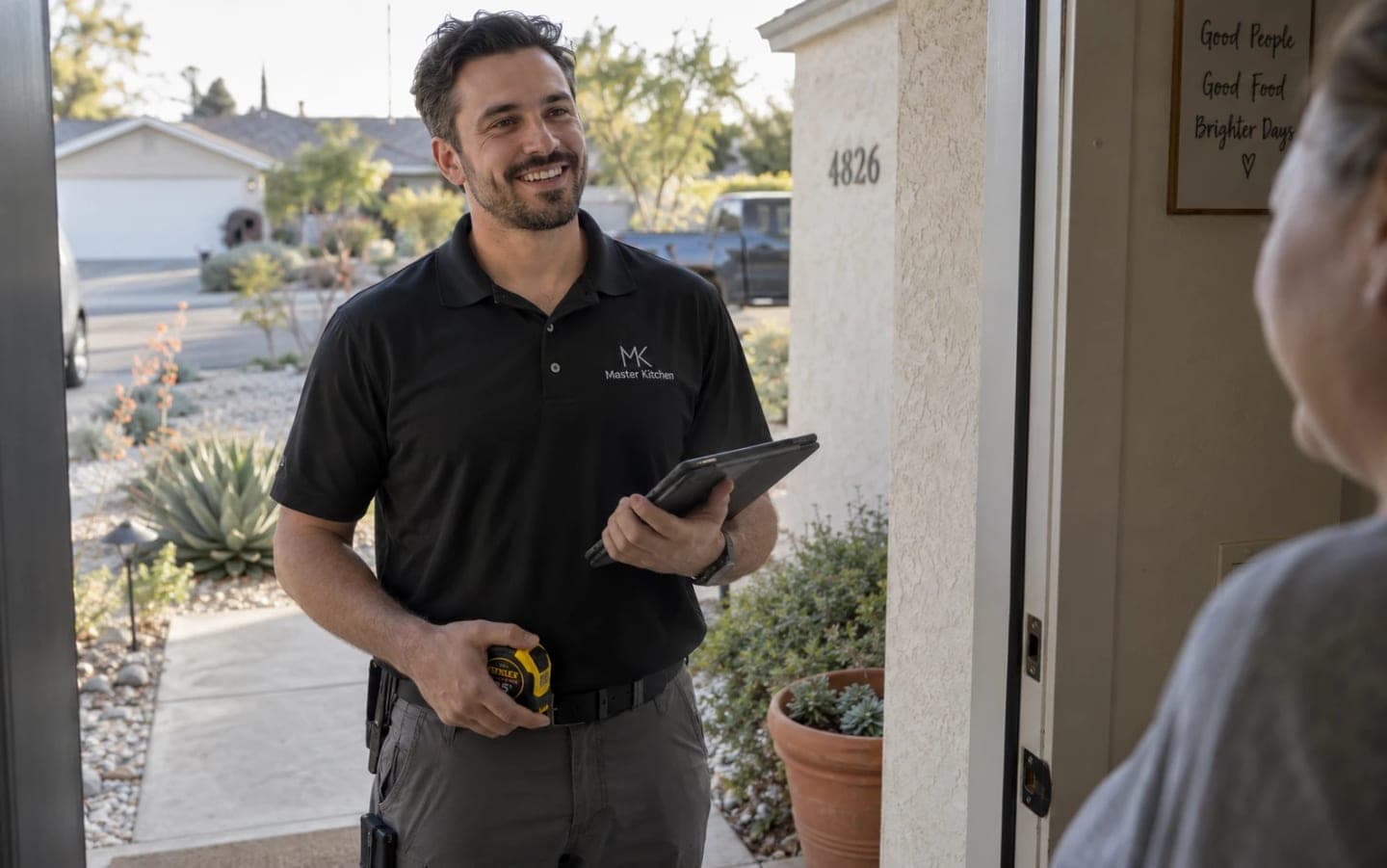 A Master Kitchen representative with a tablet and a tape measure, greeted at a homeowner's front door