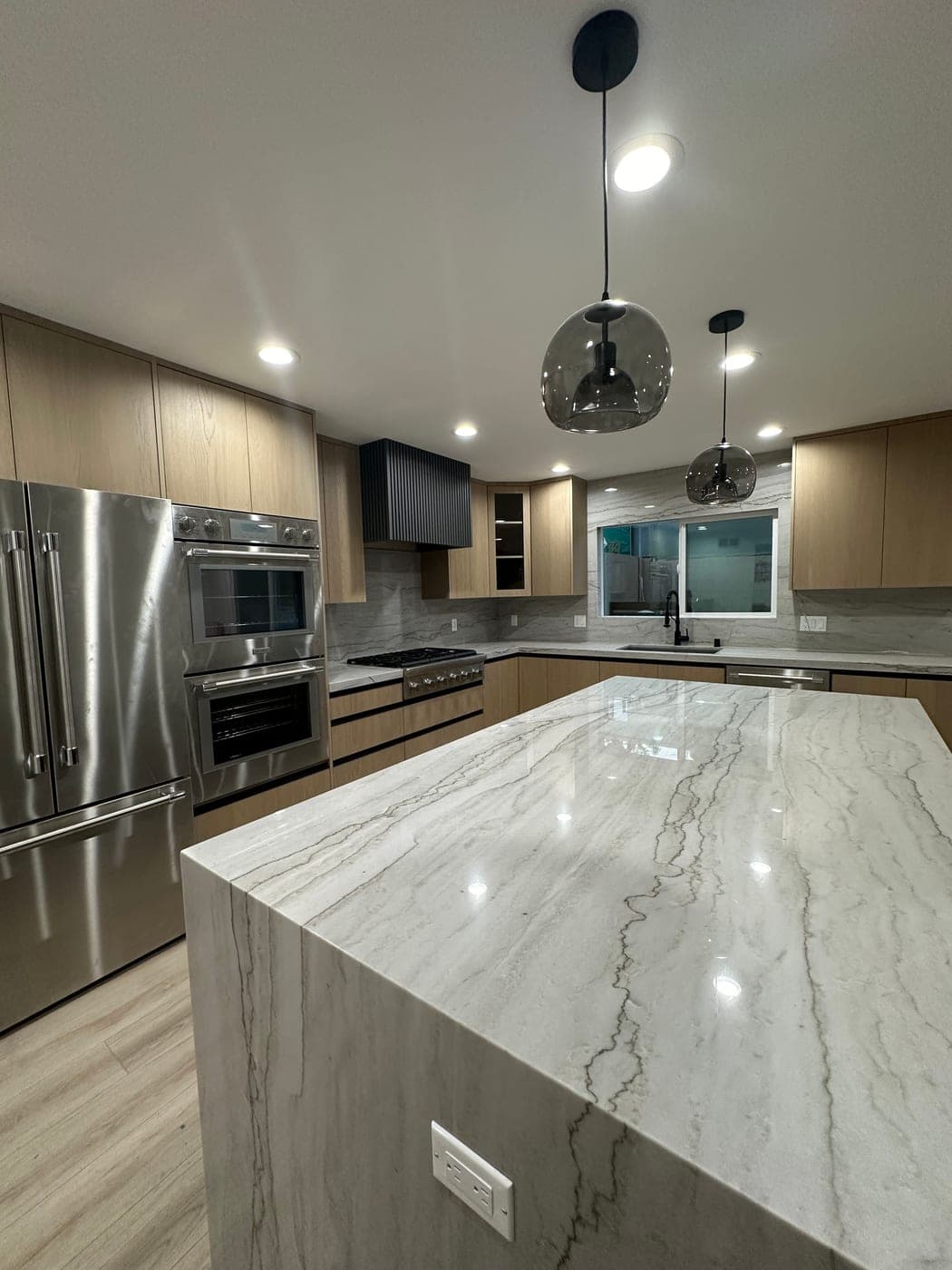 Book-matched quartzite island top with the built-in ovens and refrigerator behind