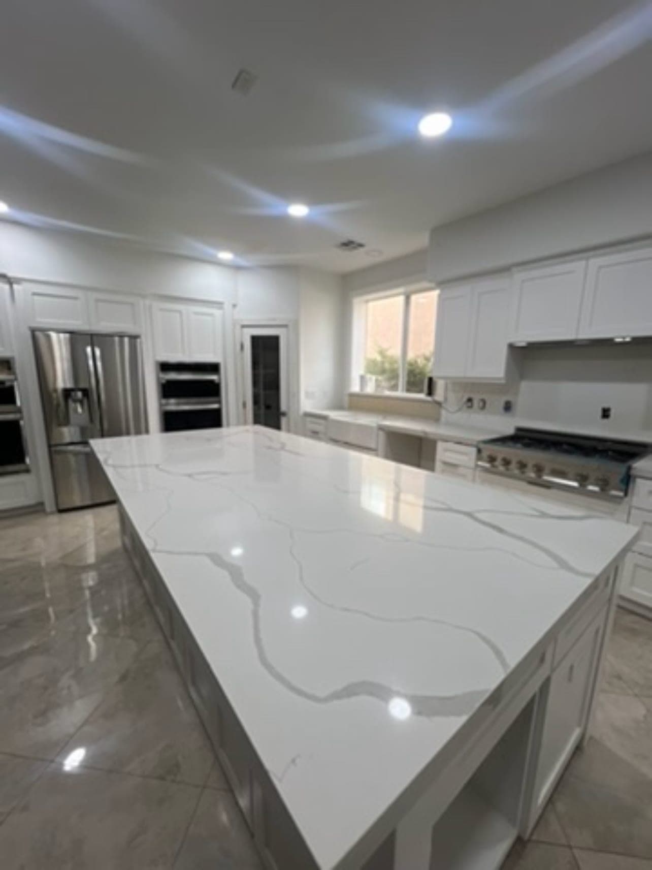 Finished kitchen: white cabinets and a large island with a white veined countertop