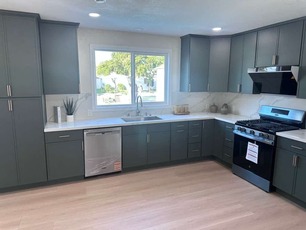 Kitchen with deep green Shaker cabinets, white marble-look countertops and backsplash, and stainless appliances