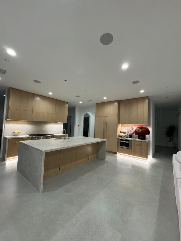Waterfall island with lit toe kicks, with light oak flat-panel cabinets behind