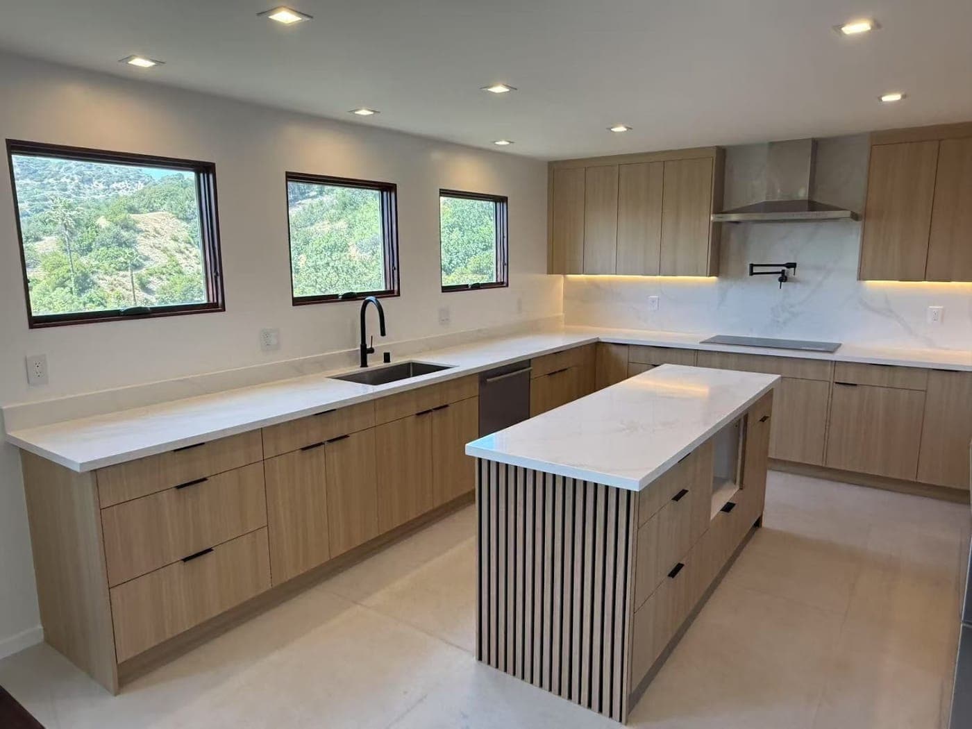 Light wood flat-panel cabinets, white countertops and a slatted island, with three windows onto the hills