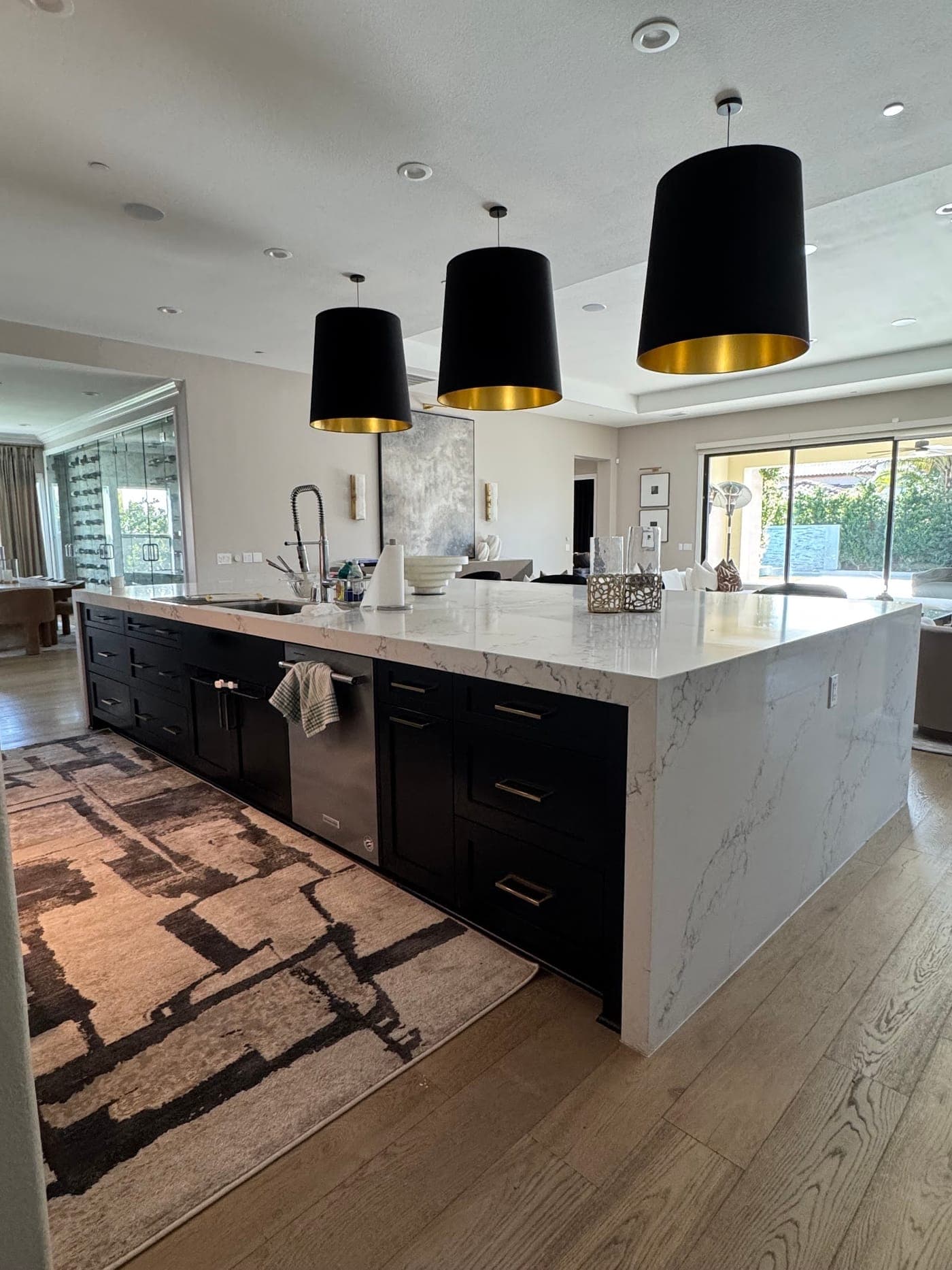 Large black island with a white veined waterfall countertop, a sink and a dishwasher, under three black drum pendants