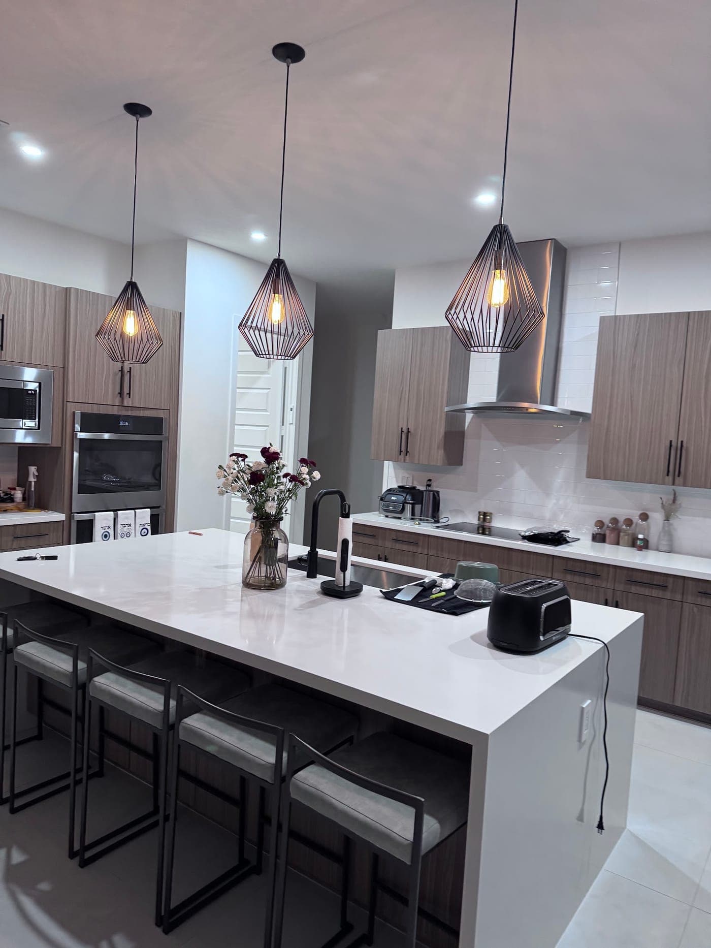 Kitchen with wood-grain flat-panel cabinets, a white waterfall island with bar stools and three geometric cage pendants