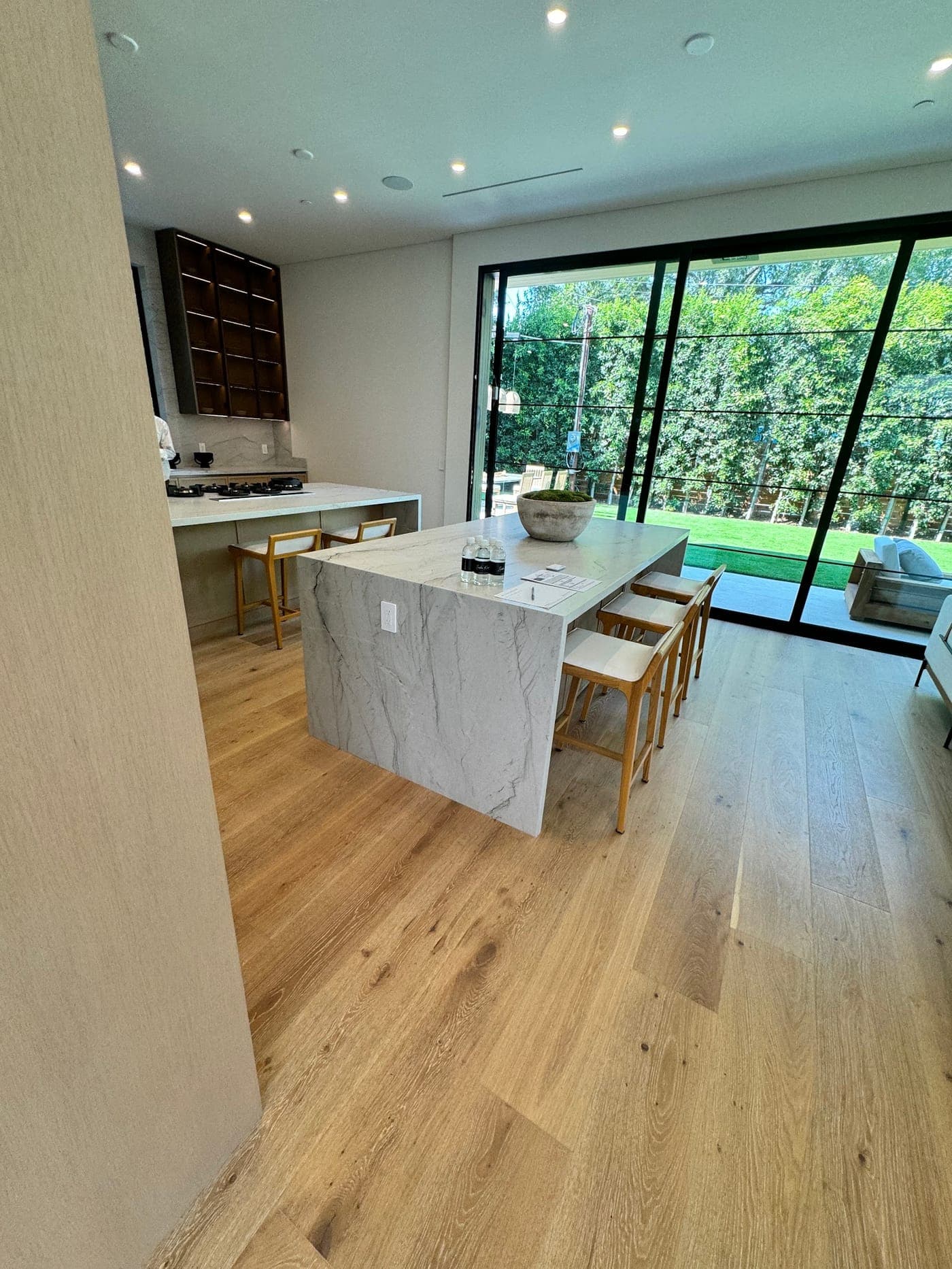 Kitchen island with a white veined waterfall countertop and stools, beside sliding glass doors to the garden
