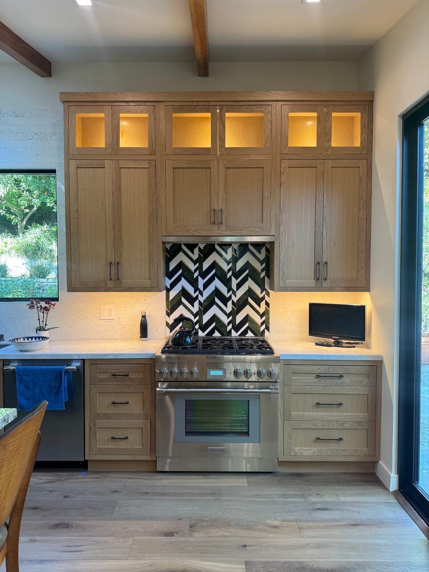Oak cabinets with lit glass uppers around a stainless range and a black and white chevron backsplash