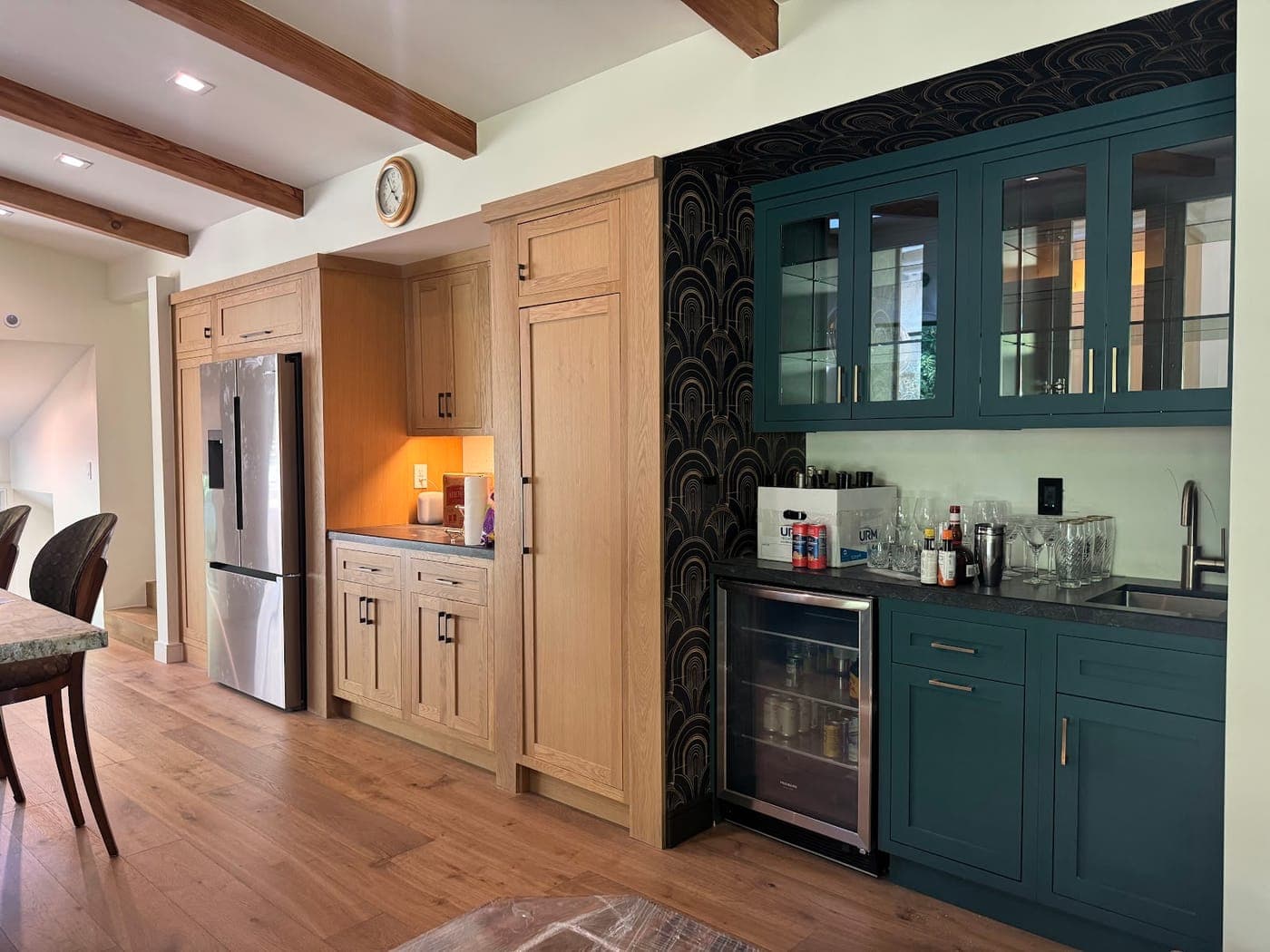 Oak cabinetry beside a teal bar with glass-front upper cabinets and a beverage fridge