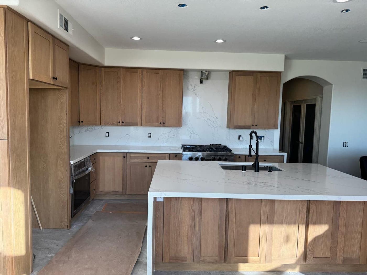 Oak Shaker cabinets, a white veined slab backsplash and an island with a waterfall countertop, with the floor still covered