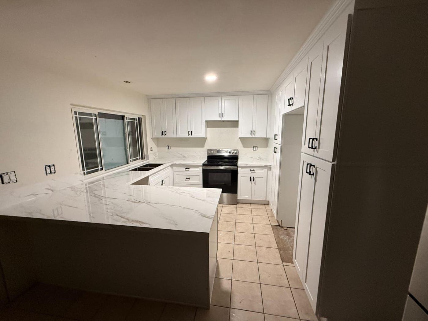 White Shaker cabinets with black pulls and marble-look countertops in a U-shaped kitchen