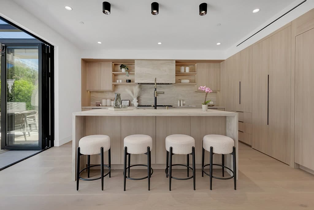 West Hollywood kitchen: oak cabinetry, a stone waterfall island with four stools and doors open to the yard