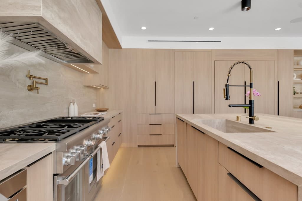 Professional range set into oak cabinetry under a stone-clad hood